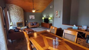 A spacious living area with a stone fireplace, a wooden dining table, and a comfortable seating arrangement. - Commander`s Cabin - Family Friendly Adventure (Sulphur)