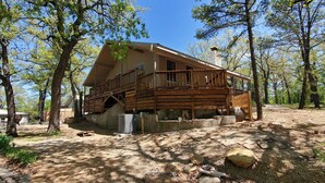 A wooden cabin with a balcony, surrounded by trees and a dirt ground. - Commander`s Cabin - Family Friendly Adventure (Sulphur)