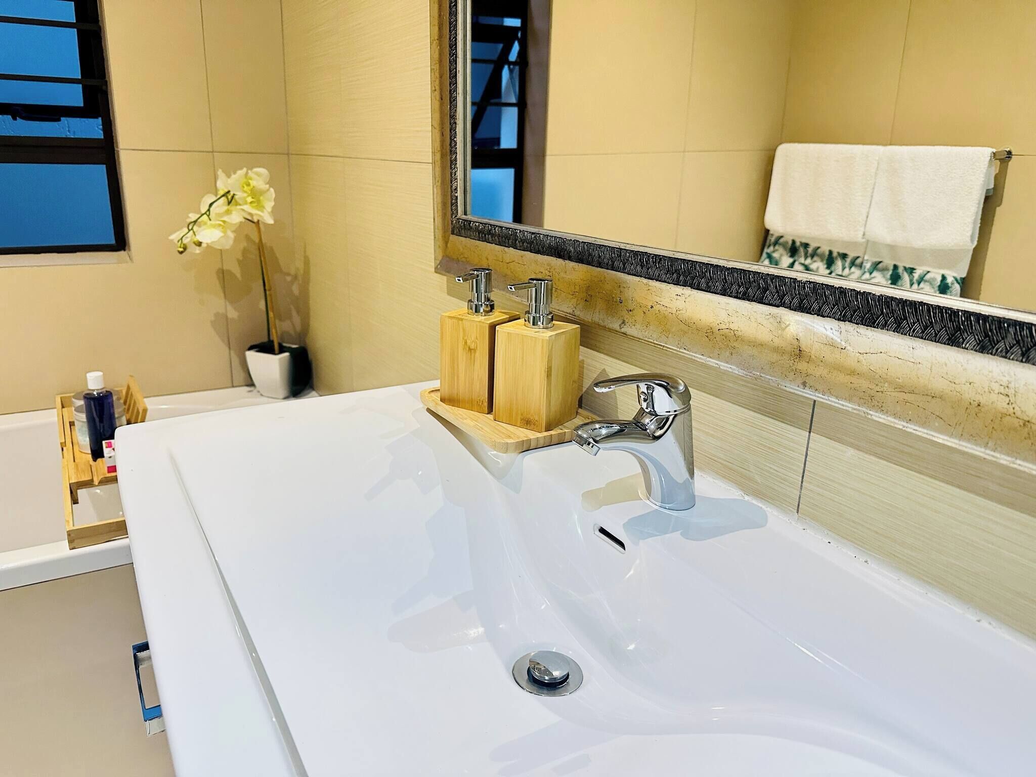 Un baño moderno con un lavamanos blanco grande, un espejo y un dispensador de jabón de madera.