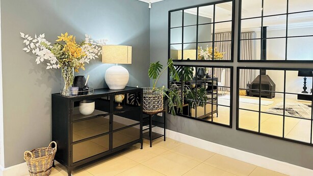 A modern living room with a black console table, a large mirror, and a view of a fireplace through a grid-patterned window. - Staycation With Back Up Power (Germiston)