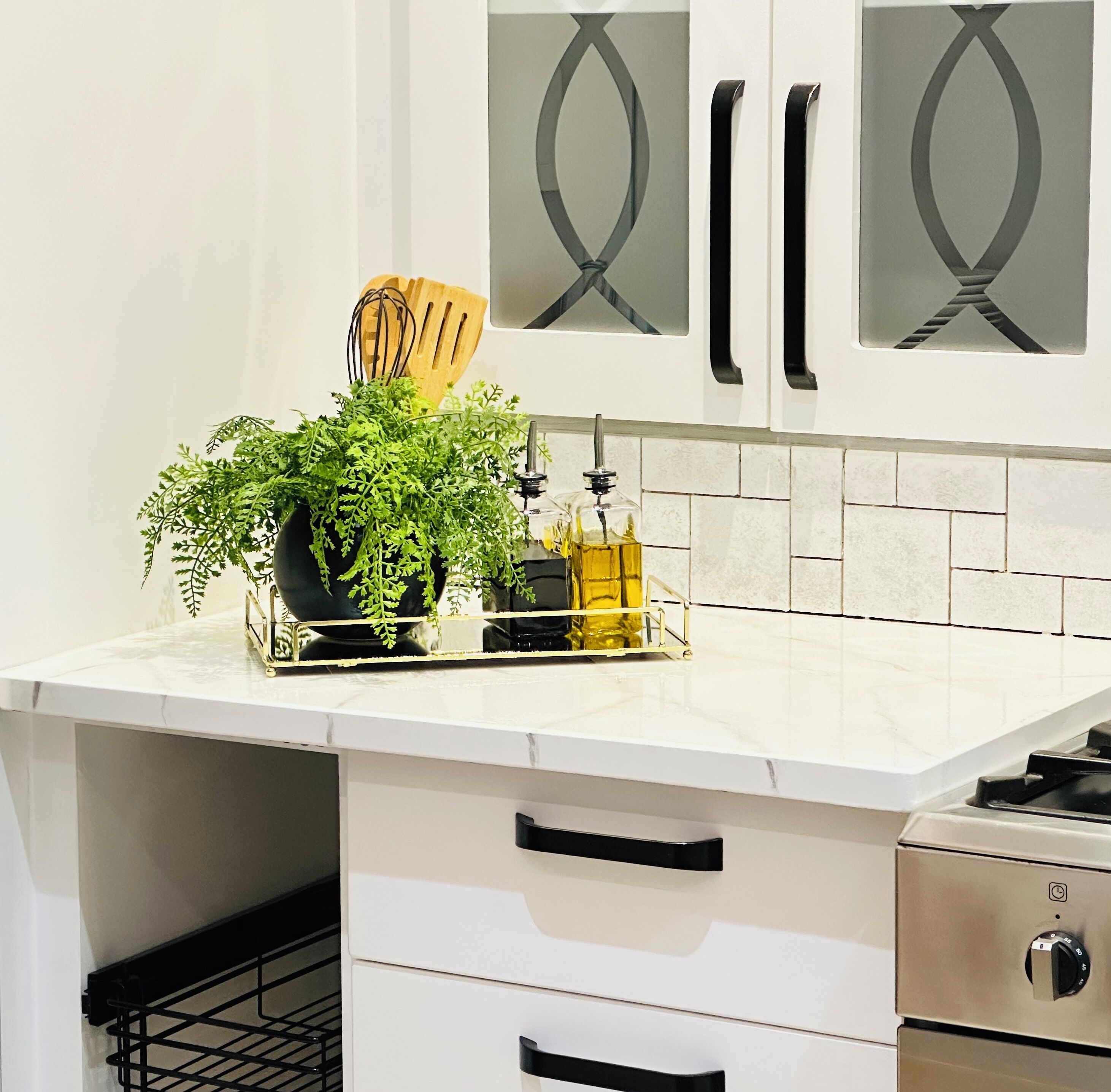 A kitchen with white cabinets, a marble countertop, a plant, a bottle of oil, and a knife block.