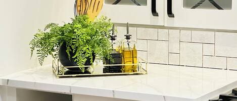 A kitchen with white cabinets, a marble countertop, a plant, a bottle of oil, and a knife block.