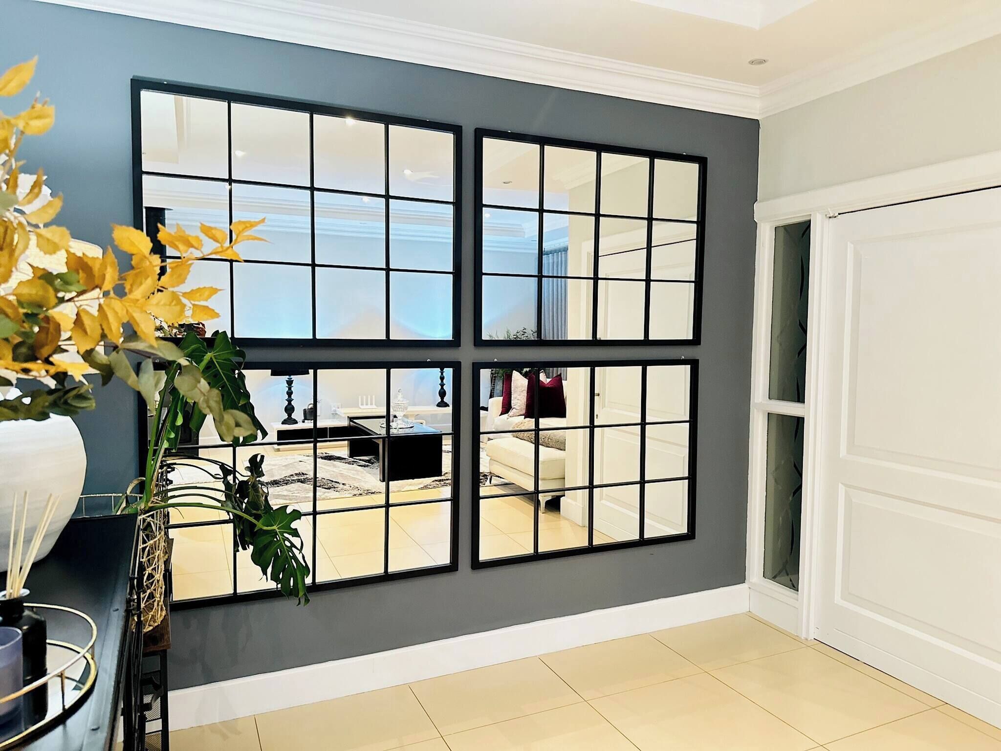 A room with a large window divided into four panes, a white door, and a plant on a table.