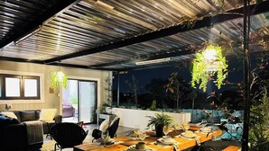 An outdoor dining area with a wooden table set for two, surrounded by plants and a hanging light fixture. - Staycation With Back Up Power (Germiston)