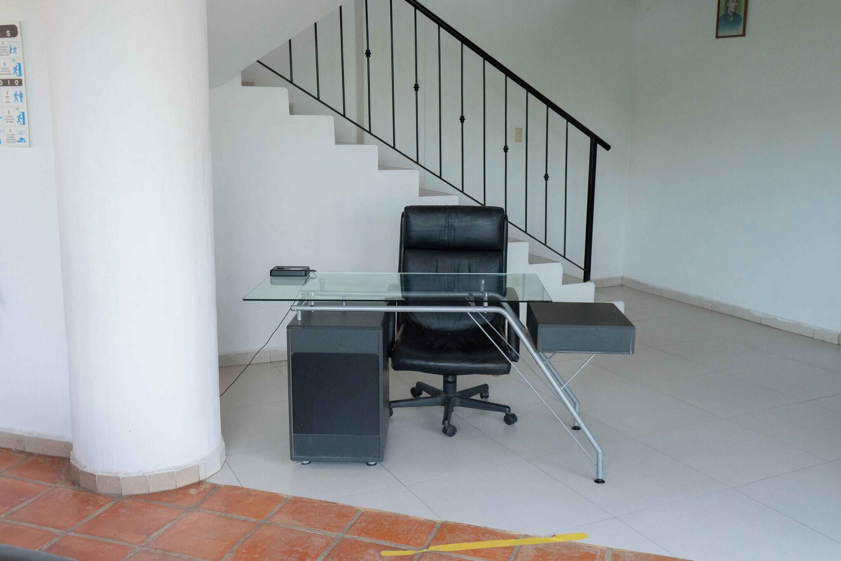 Een moderne kantoorruimte met een glazen bureau, een zwarte bureaustoel en een trap met een zwarte balustrade.