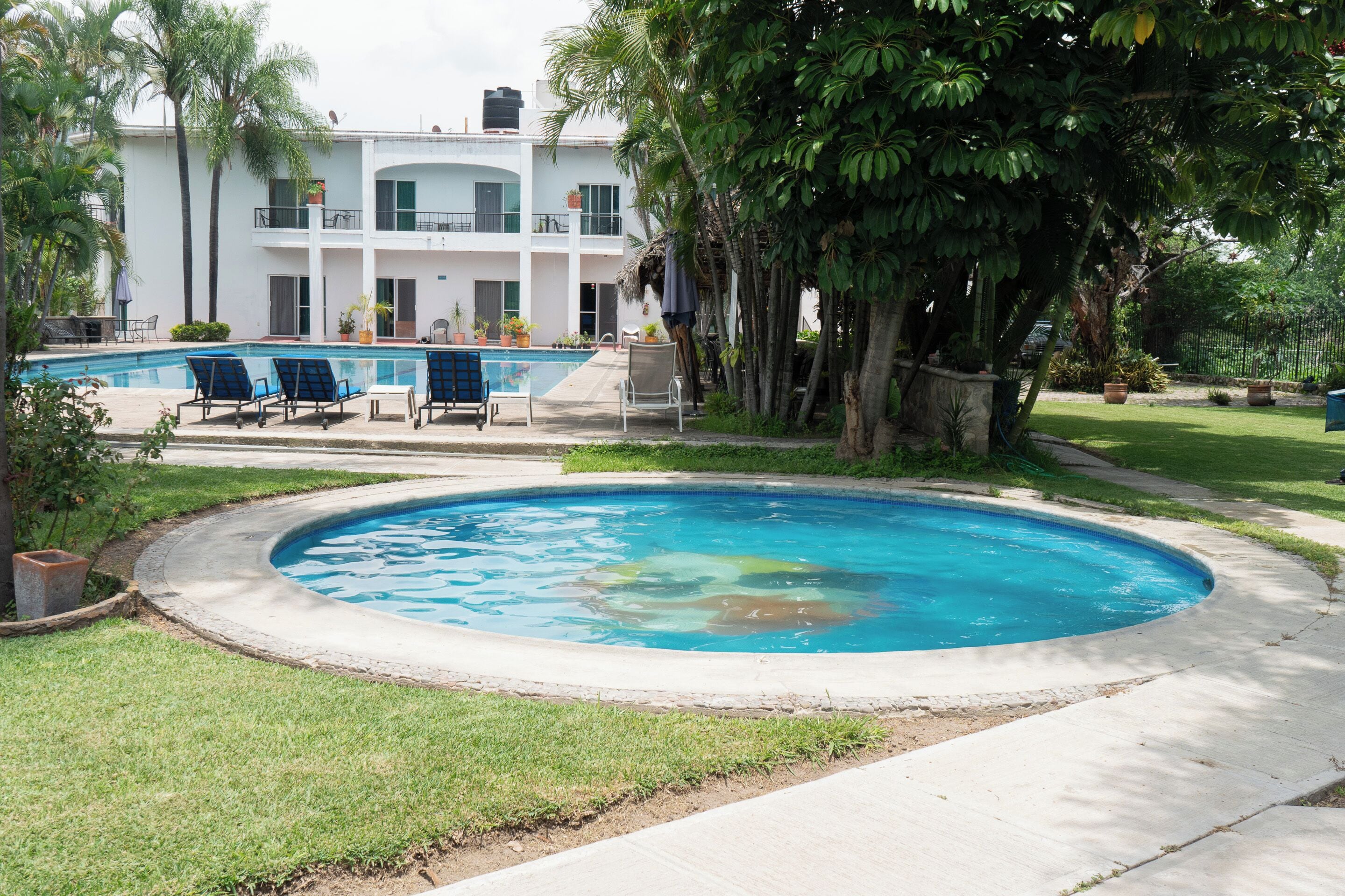 A swimming pool with lounge chairs, a building with balconies, and surrounding greenery.