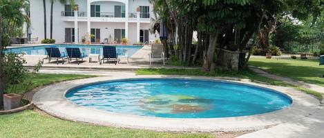 A swimming pool with lounge chairs, a building with balconies, and surrounding greenery.