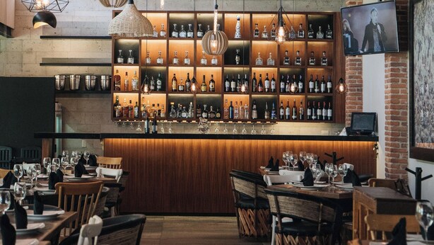 A bar area with shelves of bottles, a TV mounted on the wall, and tables set for dining. - La Joya del Lago (Chapala)