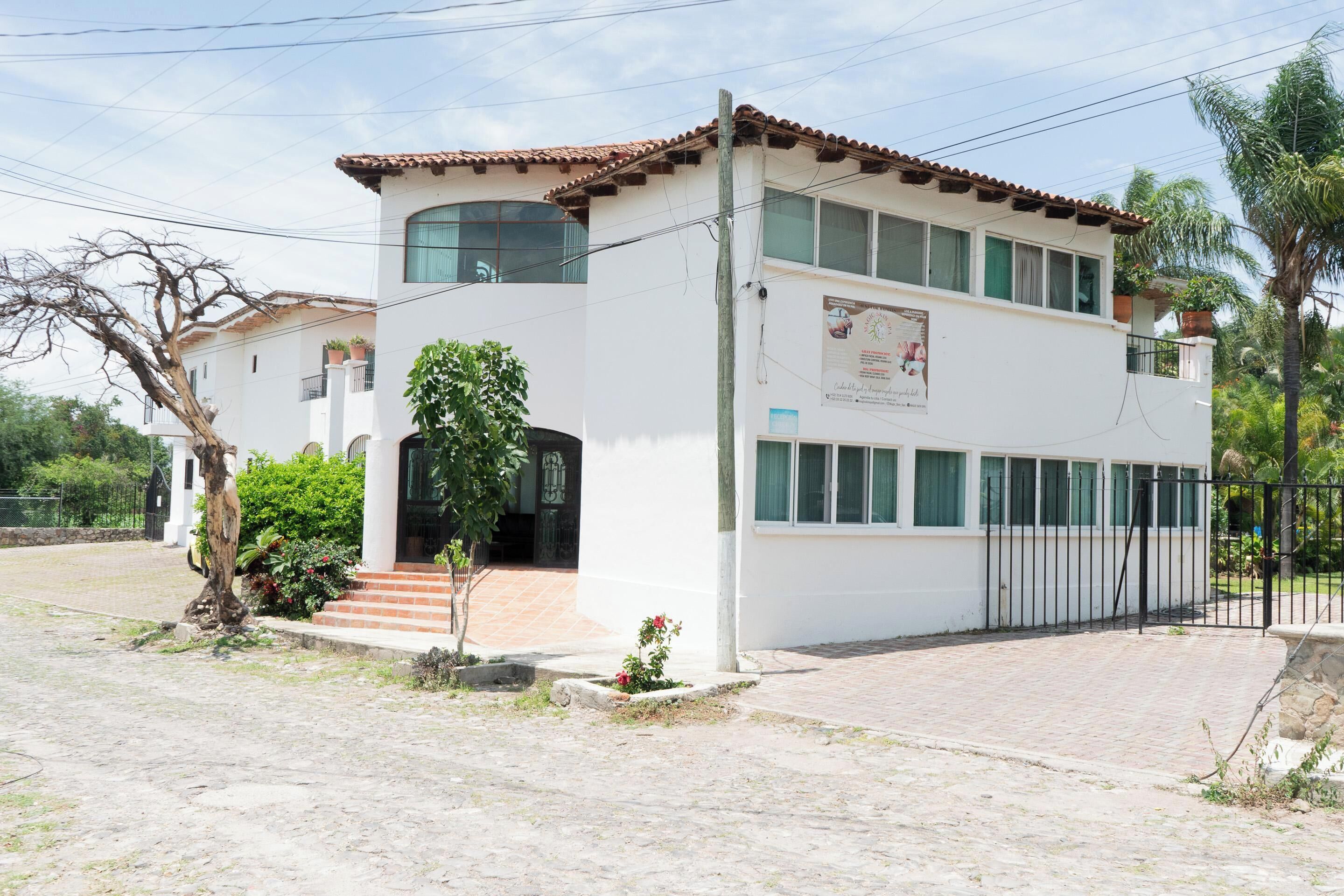 Un edificio de dos plantas con techo de tejas, balcón y entrada pavimentada.