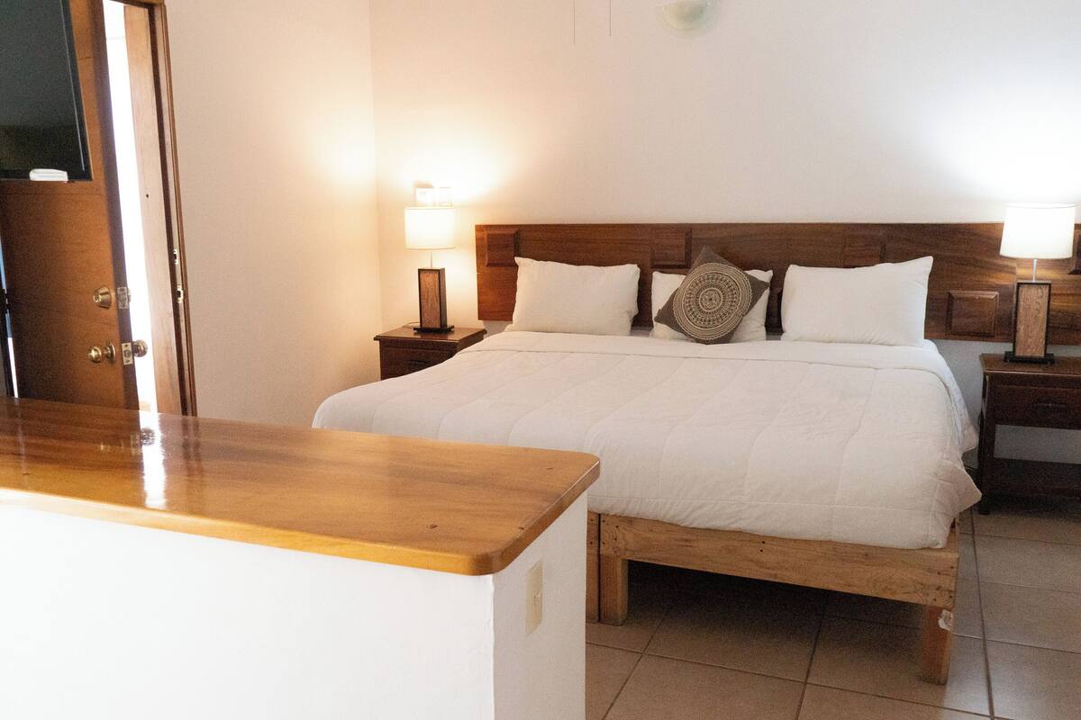 A bedroom with a wooden bed, white bedding, two bedside tables with lamps, and a wooden nightstand.