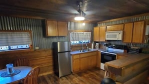 A compact kitchen with wooden cabinets, a refrigerator, a stove, and a sink.