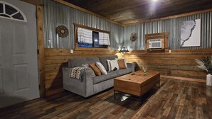 A cozy room with a wooden floor, a grey sofa with patterned cushions, a wooden coffee table, and a wall-mounted air conditioning unit.