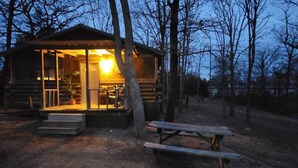 A rustic cabin with a porch and a picnic table, surrounded by trees.