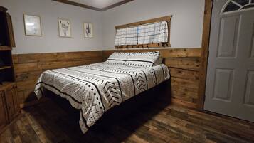 A bedroom with a bed, wooden walls, a window with curtains, and a door.