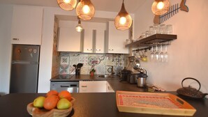A kitchen with a modern design, featuring a stainless steel refrigerator, a sink, and a variety of kitchen utensils. There are hanging lights and a shelf with glasses.