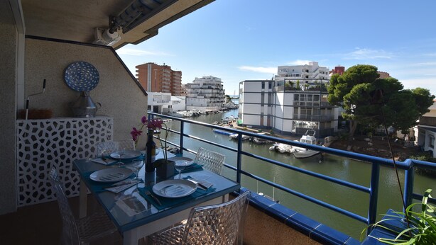 A balcony with a table set for dining, overlooking a marina with boats and buildings.