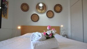 A neatly made bed with a towel and a bouquet of flowers, a wooden headboard, and decorative plates on the wall.