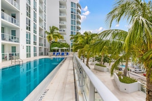 Um hotel moderno com piscina, varandas e palmeiras.