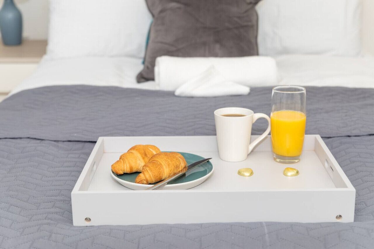 A breakfast tray with croissants, a cup of coffee, and a glass of orange juice on a bed.