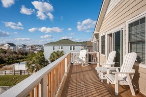 A wooden deck with white Adirondack chairs, a small table, and a view of neighboring houses.