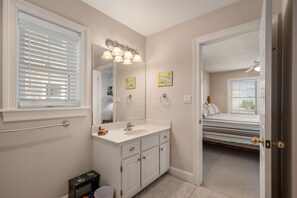 A bathroom with a white vanity, a mirror, and a window with blinds.