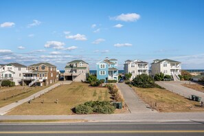 A row of beachfront houses with a clear view of the ocean, a paved walkway, and a road in the foreground.