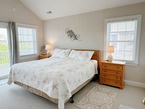 Quarto com cama grande, duas mesas de cabeceira com abajures, um painel decorativo e vista pela janela.