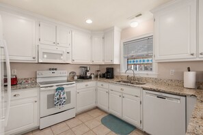 A kitchen with white cabinets, a stainless steel sink, a Bosch dishwasher, and a window with blinds.