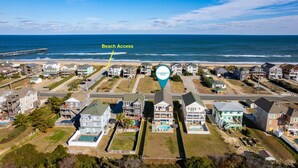 An aerial view of a coastal residential area with houses, a pier, and a marked beach access point. - Pelican's Post: Semi-Oceanfront, Private Pool, Hot Tub and Game Room (Nags Head)