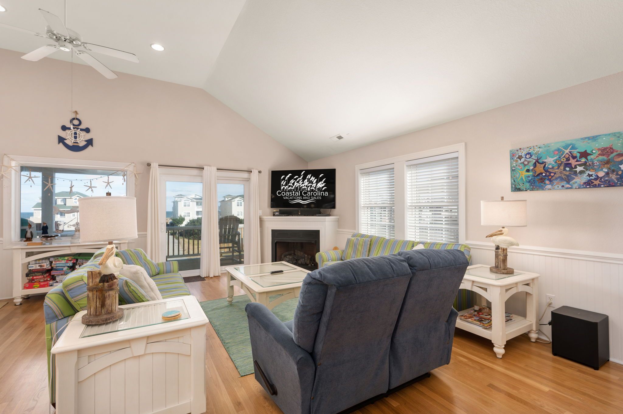 A living room with a fireplace, a television, and a view of the ocean through large windows.