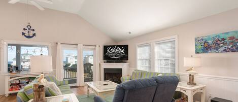 A living room with a fireplace, a television, and a view of the ocean through large windows.