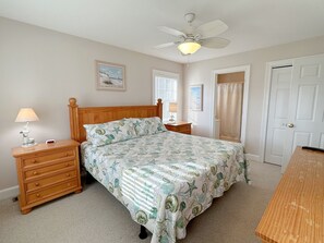 A bedroom with a bed, a nightstand, a lamp, a ceiling fan, a door, and a window with blinds.