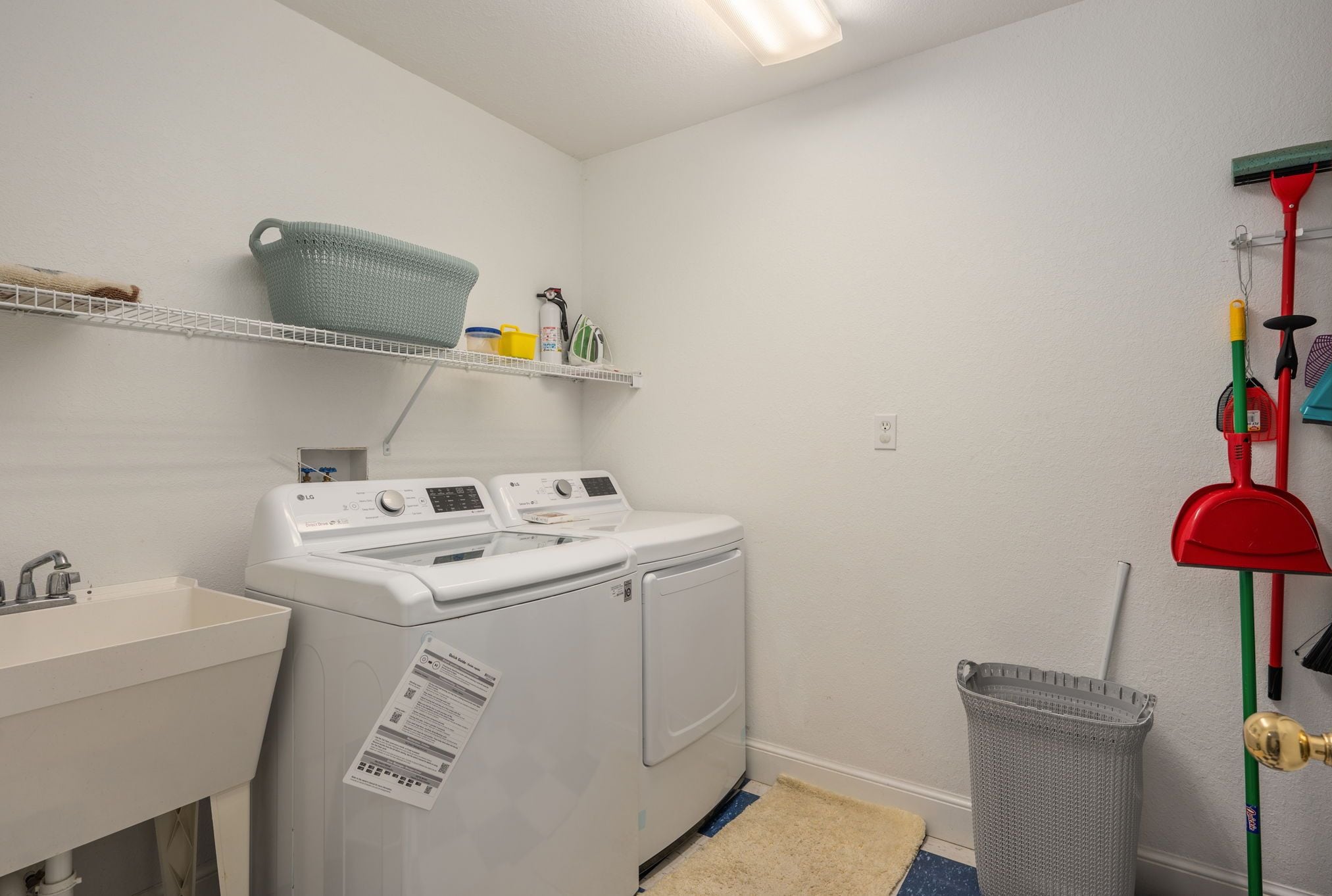 Een wasserette met een wasmachine, een wasbak, planken met wasmiddelen en schoonmaakspullen.