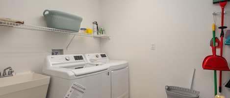 Een wasserette met een wasmachine, een wasbak, planken met wasmiddelen en schoonmaakspullen.