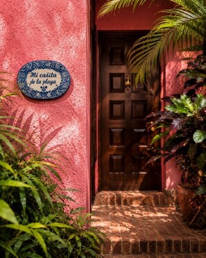 Pared vermelha com um prato decorativo, uma porta de madeira e um caminho de tijolos.