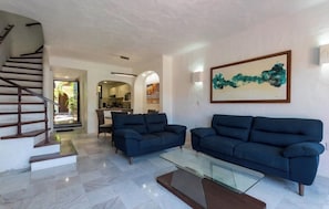 Uma sala de estar com escada, dois sofás, uma mesa de centro de vidro e um quadro na parede.