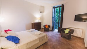 A bedroom with a bed, a dresser, a chair, a TV, and a window with an open door leading to a balcony. - Villa Afrodite 8 Emma Villas (Milazzo)