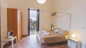 A bedroom with a four-poster bed, a bedside table with a lamp, a TV on a stand, and a view of a balcony with outdoor furniture. - Villa Afrodite 8 Emma Villas (Milazzo)