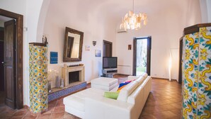 A living room with a fireplace, a television, a sofa, and a patterned column. - Villa Afrodite 8 Emma Villas (Milazzo)