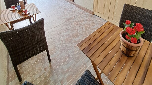 Un área de patio con una mesa y sillas de madera, una maceta con flores rojas y un paraguas grande.