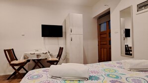 Un dormitorio con cama, escritorio, silla, televisor y puerta.