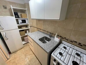 Eine kompakte Küche mit Gasherd, Mikrowelle, Spüle und Kühlschrank.