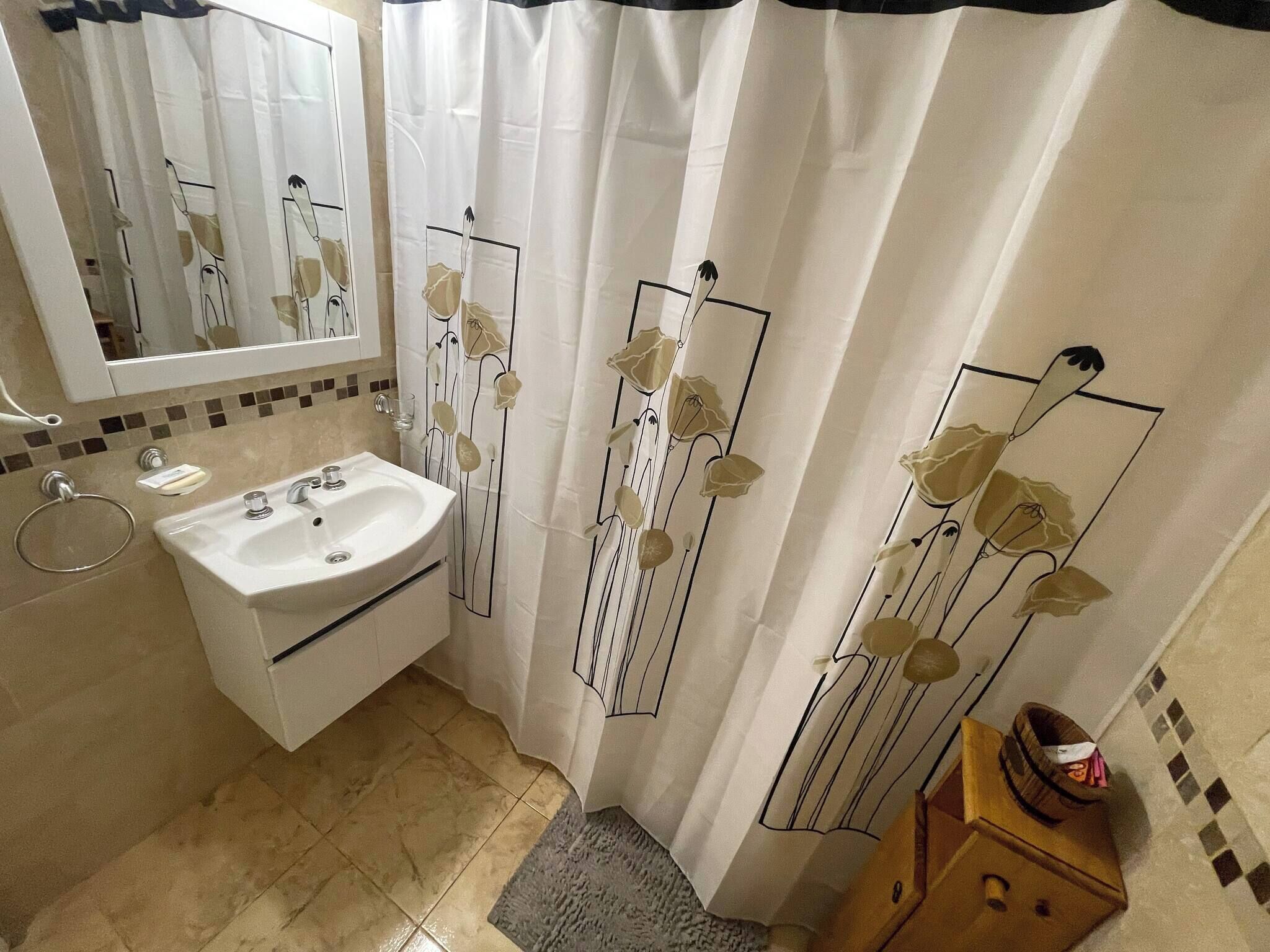 Un baño con lavamanos, espejo y cortina de ducha con motivos florales.