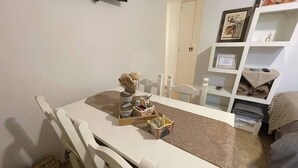 Ruokailutila, jossa on pöytä, tuoleja, pieni koiran hahmo ja hylly, jossa on taiteltuja peittoja.