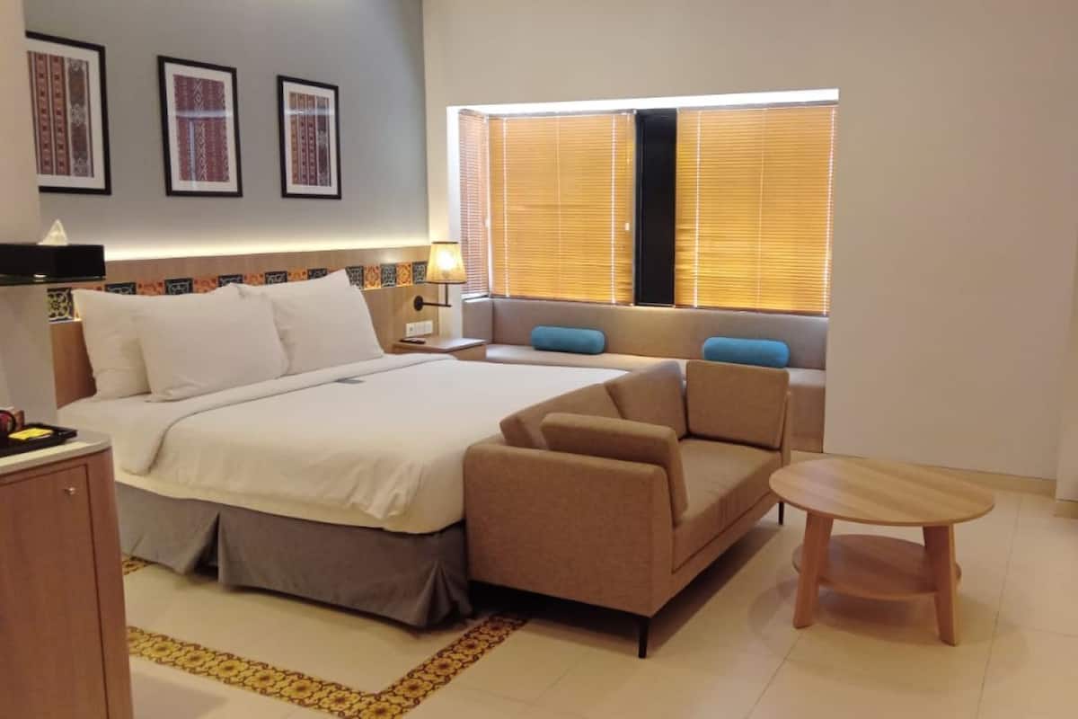 Une chambre d’hôtel moderne équipée d’un lit, d’un canapé, d’une petite table et d’une fenêtre avec des stores.