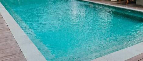 A rectangular pool with wooden deck flooring, surrounded by lounge chairs and umbrellas.