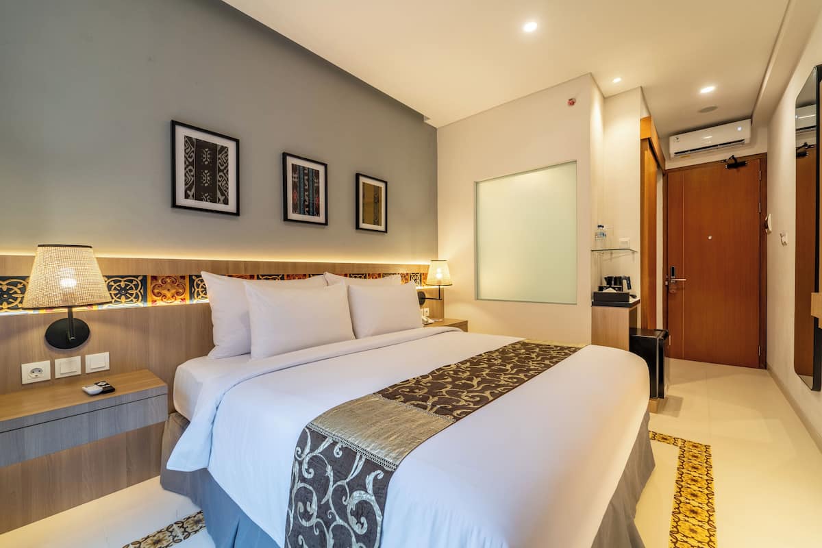 Une chambre d’hôtel moderne avec un grand lit, une table de chevet, une lampe, des tableaux encadrés au mur et un appareil de climatisation.