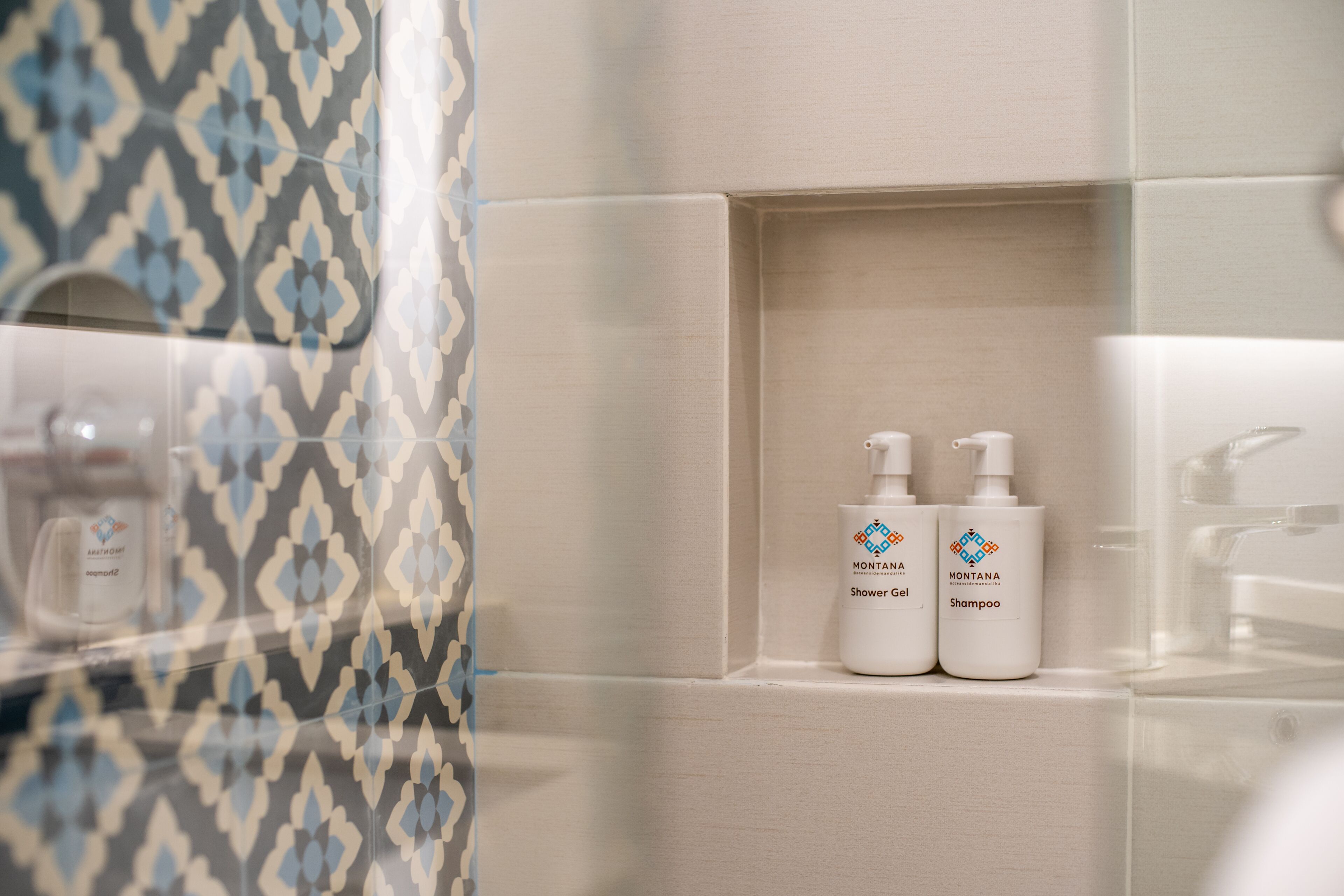 A bathroom with patterned tiles, a shower, and two bottles of Montana shower gel and shampoo on a shelf.