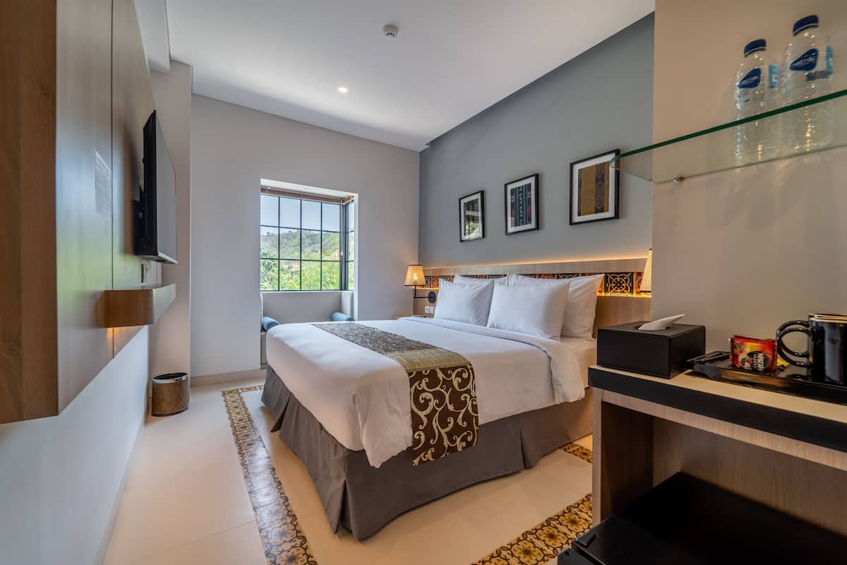 Une chambre d’hôtel moderne, dotée d’un grand lit, de tables de chevet, d’une télévision et d’une fenêtre offrant une vue agréable.