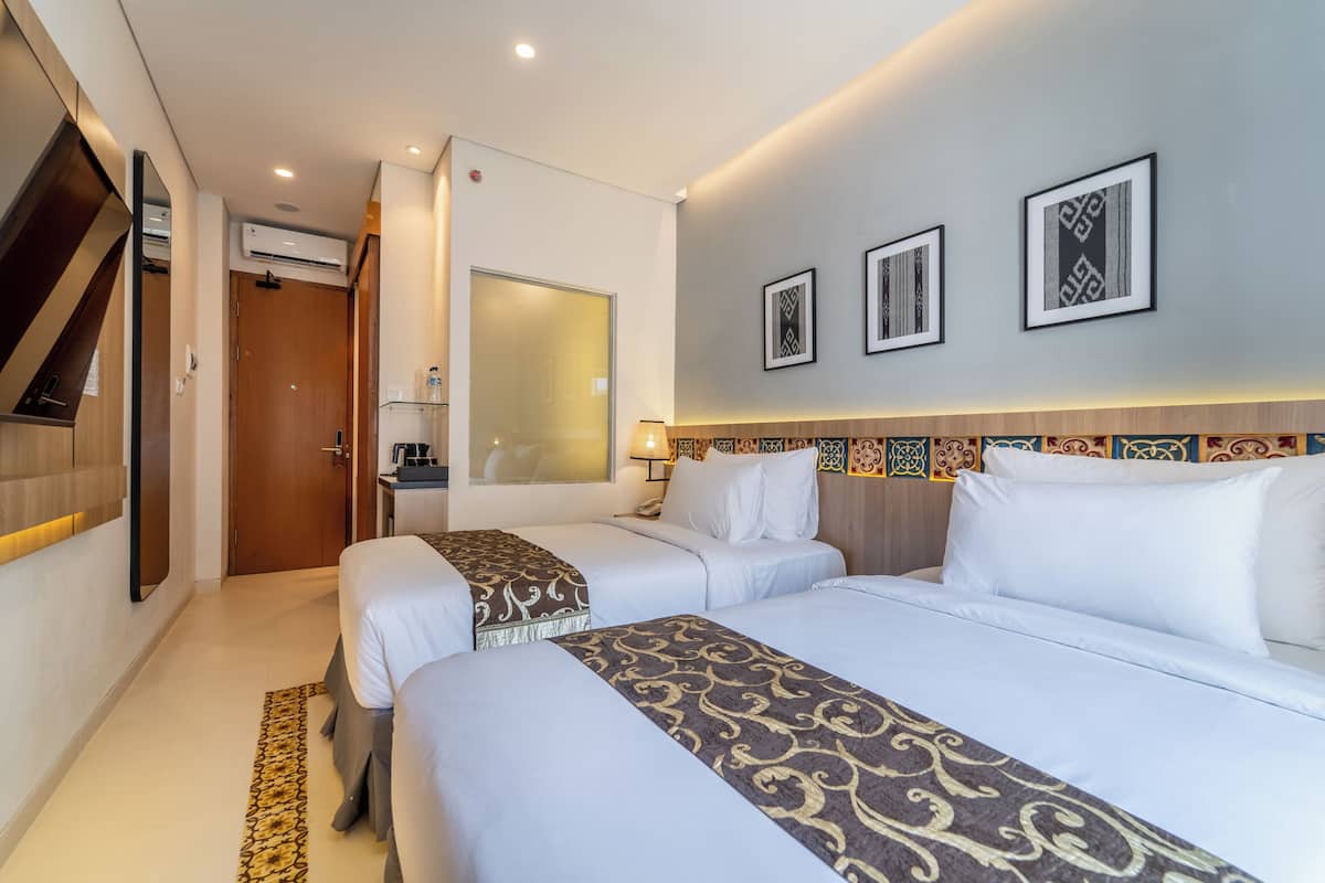 Une chambre d’hôtel avec deux lits, un miroir, un bureau et un téléviseur fixé au mur.